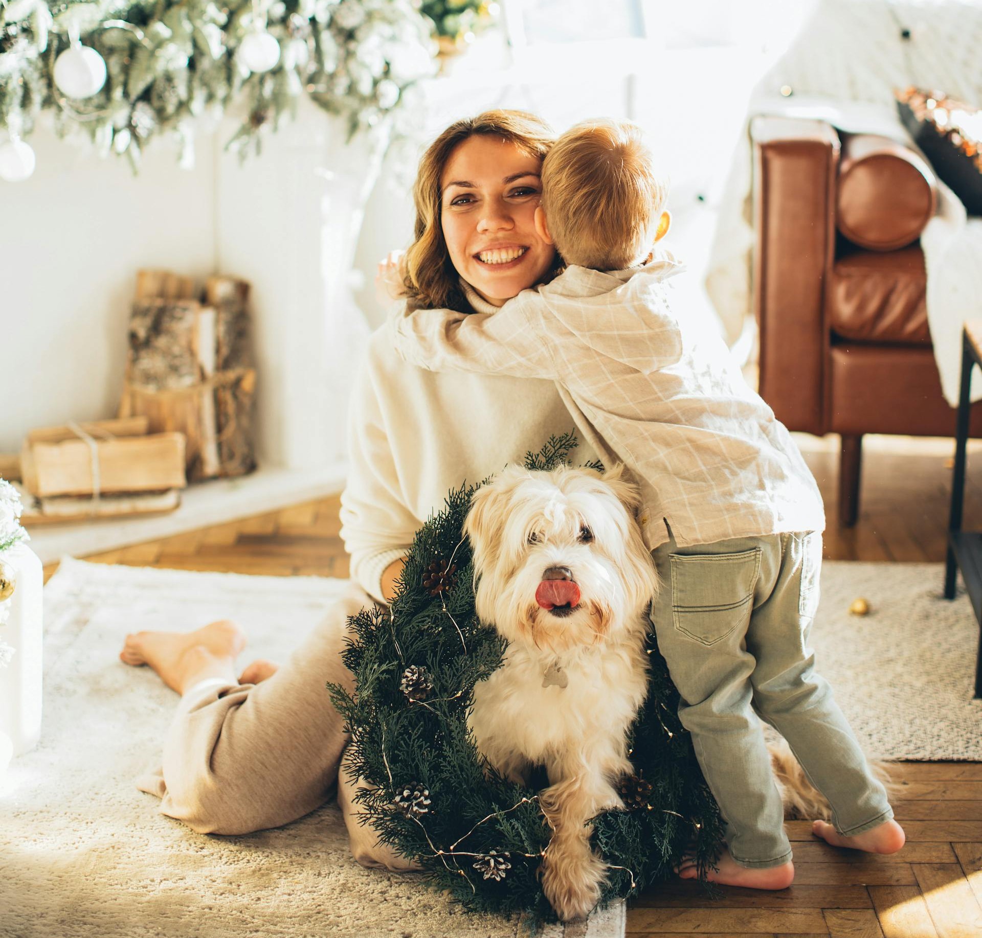 A woman and her child with a dog, surrounded by presents in front of a beautifully lit Christmas tree.